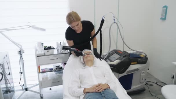 Cosmetologist de movimento lento com equipamento especial faz o procedimento de laser da remoção de vasos sanguíneos na cara de meninas — Vídeo de Stock