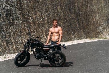 Onun motosiklet yakın poz kot çıplak vücut ile seksi adam, arka planda kayalar.