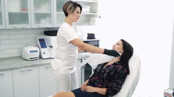 Женщина на приеме у косметолога, замедленная съемка. Косметолог готовит пациента к косметической процедуре — стоковое видео