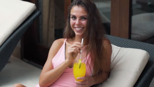 Beautiful girl in a swimsuit looks into the camera, smiles and drinks orange juice, slow motion. — Stock Video