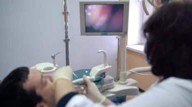 Kadın diş hekimi ağız içi kamera ile hastanın dişlerini inceler ve sonuçları monitörde görüntüler.
