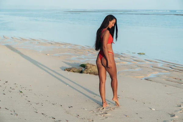 Портрет красивої сексуальної дівчини в червоному купальнику з довгим волоссям позує на пляжі з білим піском — стокове фото