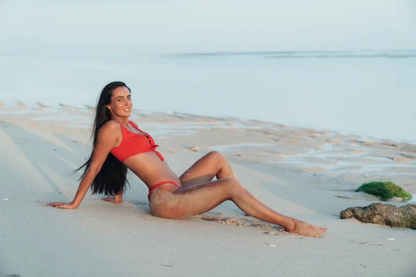 Porträt eines schönen Mädchens mit langen Haaren im roten Badeanzug am Strand mit weißem Sand liegend — Stockfoto