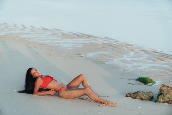 Портрет красивої дівчини з довгим волоссям у червоному купальнику, що лежить на пляжі з білим піском — стокове фото