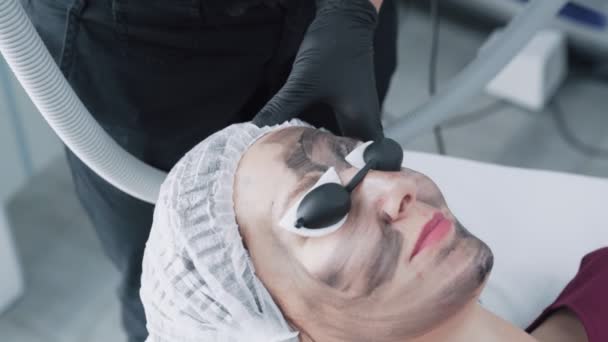 Крупный план руки косметолог делает процедуру пилинга углерода на лице молодой женщины в клинике, замедленная съемка — стоковое видео