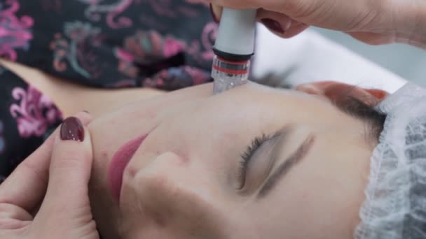 Крупним планом косметологічні руки роблять процедуру гідравлічного пілінгу на обличчі жінки з медичним пристроєм, повільний рух — стокове відео