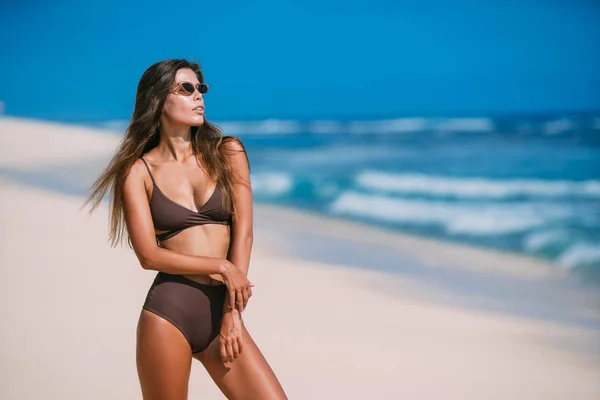 Σέξι μαυρισμένο μοντέλο με τα γυαλιά ηλίου σε καφέ μαγιό ποζάρει στην παραλία λευκή άμμο — Φωτογραφία Αρχείου