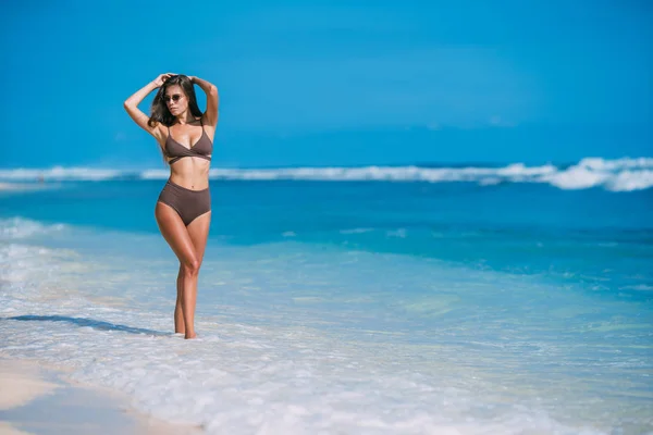 Beautiful tanned girl posing on beach with white sand and blue ocean. — Stock Photo, Image