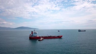 Su üzerinde kırmızı tanker gemisi havadan görünümü, yakın çekme gemisi, limana giriş