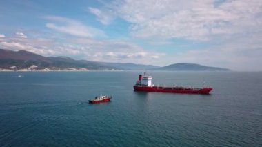 Su üzerinde kırmızı tanker gemisi havadan görünümü, yakın çekme gemisi, limana giriş