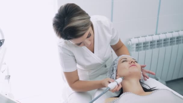 Beautician does moisturizing and tightening procedure on face of young woman in clinic, slow motion — Stock Video