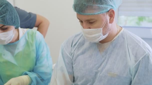 Retrato de dois médicos e enfermeira em máscaras e roupas estéreis durante a cirurgia na sala de cirurgia — Vídeo de Stock