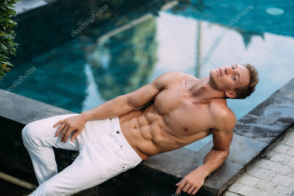 Hombre sexy sin camisa en pantalones blancos con cuerpo atlético posando en la piscina. Modelo masculino de deportes musculares — Foto de stock © rmano.mail.ru #262244086