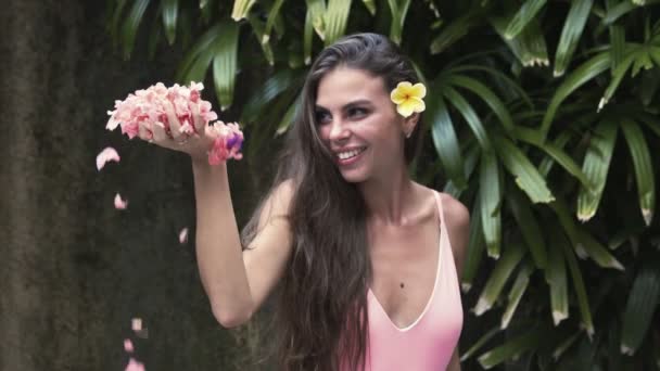 Retrato de menina feliz em maiô com flor no cabelo e pétalas na mão. câmara lenta — Vídeo de Stock