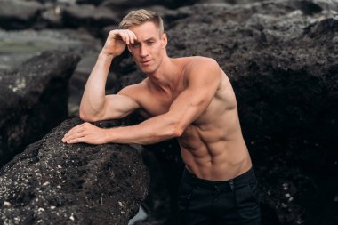 Çıplak göğüslü seksi adamın portresi siyah kumla sahilde yatıyor