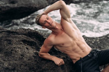 Çıplak göğüslü seksi adamın portresi siyah kumla sahilde yatıyor