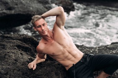 Çıplak göğüslü seksi adamın portresi siyah kumla sahilde yatıyor