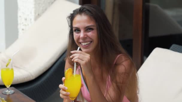 积极的女孩与一个美丽的微笑在泳衣拿着玻璃与果汁在手，慢动作. — 图库视频影像