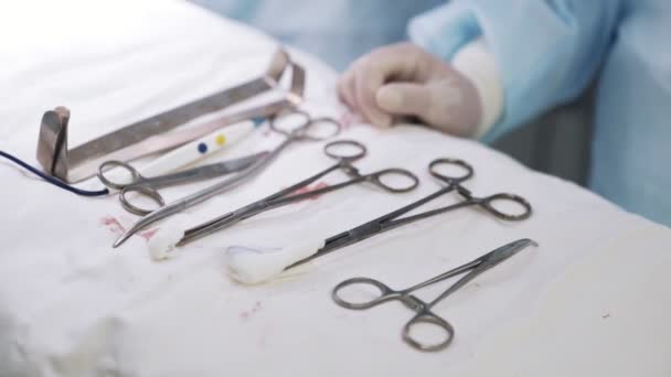 Acercamiento de instrumentos médicos, abrazaderas en bandeja estéril, la mano del médico toma uno de ellos durante la cirugía — Vídeo de stock