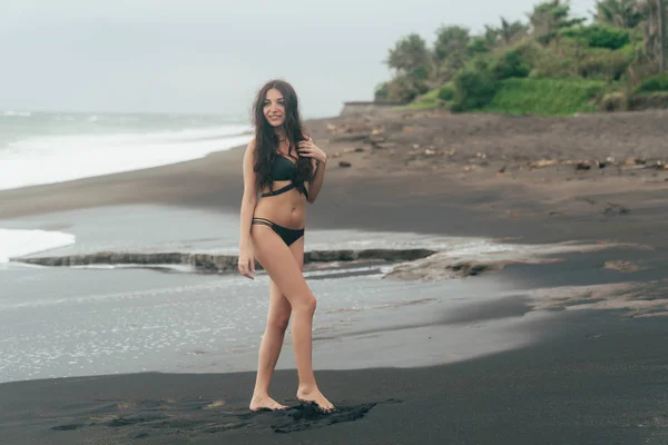 섹시 한 미소 갈색 머리 소녀 에 수영복 포즈 에 검정 모래 해변. — 스톡 사진