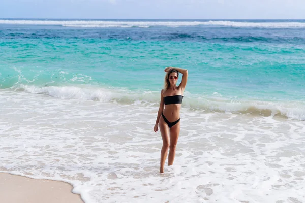 Vacker flicka i svart baddräkt och solglasögon vila nära havet på stranden — Stockfoto