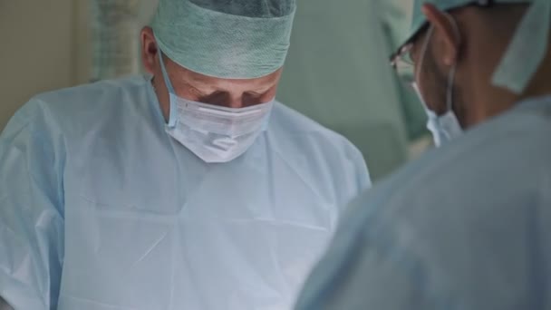 Deux médecins en vêtements stériles et masque pendant la chirurgie. Chirurgien en salle d'opération. Vue de derrière — Video