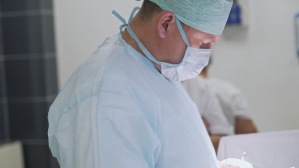 Retrato de vista lateral del médico con ropa estéril y máscara durante la cirugía. Cirujano en quirófano — Vídeo de stock