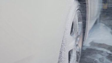 Yakın çekim, araba yıkama, detaylandırma. Araba tekerleği sabun ve su ile yıkanıyor. Yavaş çekim