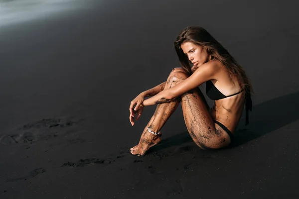 Attraente ragazza sexy in costume da bagno riposa sulla spiaggia di sabbia vulcanica nera . — Foto Stock