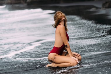 Kırmızı mayo büyük göğüsler ile seksi model siyah kum plajda pozlar.