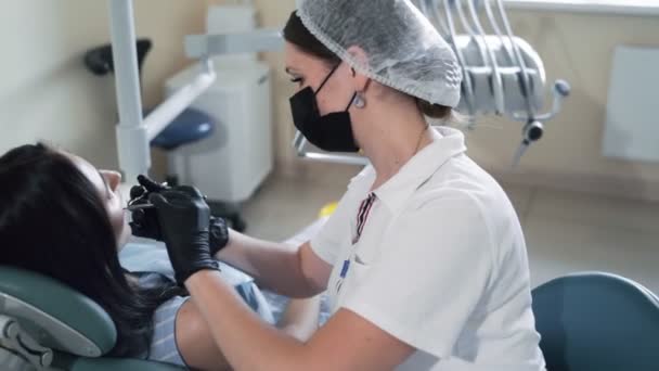 Вид сбоку, стоматолог осматривает женские зубы с помощью стоматологических инструментов, замедленная съемка — стоковое видео