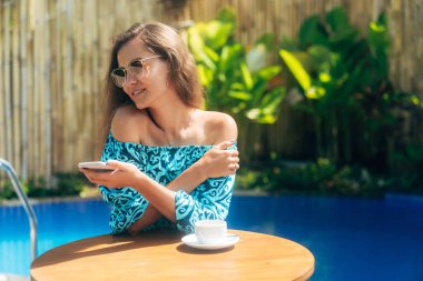 Güneş gözlüğü güzel model çay veya kahve fincan ı ile masada açık havada oturur ve telefon kullanır