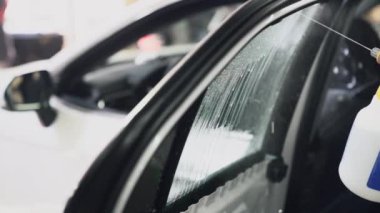 Araba camı için tint filmi takmadan önce köpük döken yakın çekim işçi, yavaş hareket.