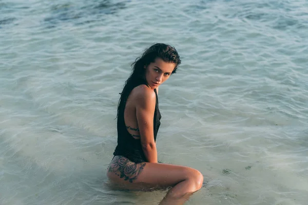 Portrét sexy brunetky v bikinách a pletených svetru na pláži, tetování na hýždí. — Stock fotografie