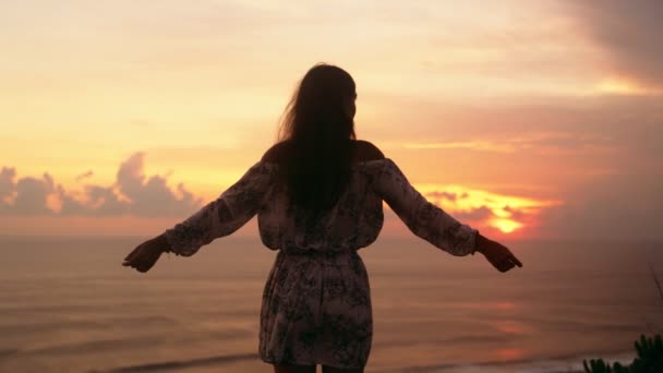 広い開かれた腕を持つ女の子のシルエットは、背景に夕日、崖の上に立っています。スローモーション — ストック動画