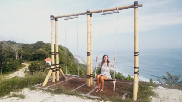 Boldog lány lengő a swing over szikla, gyönyörű kilátás az óceánra, lassított — Stock videók