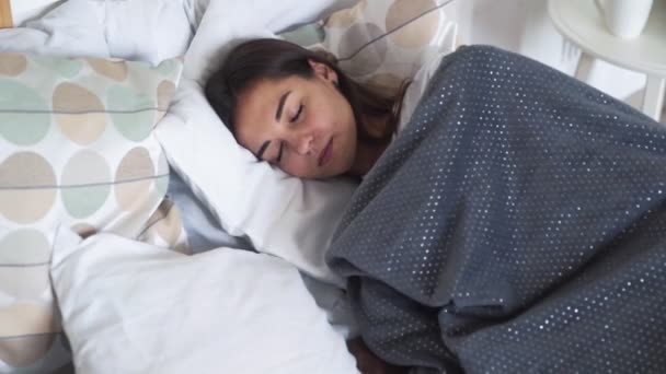 Жінка спокійно спить у ліжку, загорнута в ковдри під час снів, повільний рух — стокове відео