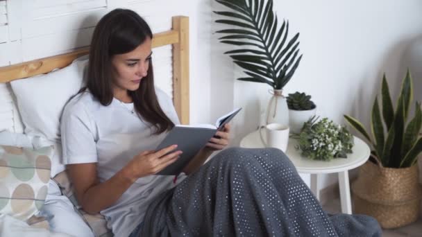 Güzel kız yatakta yatıyor ve kitap okur, yavaş hareket — Stok video