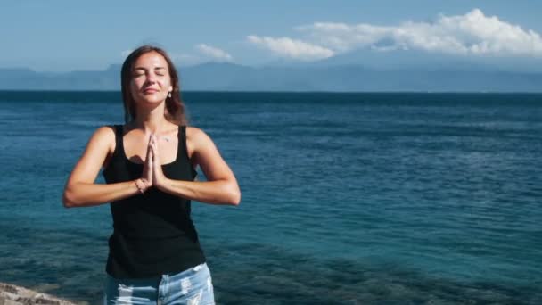 Portrait of girl meditates with closed eyes, ocean on background, slow motion — Stock Video
