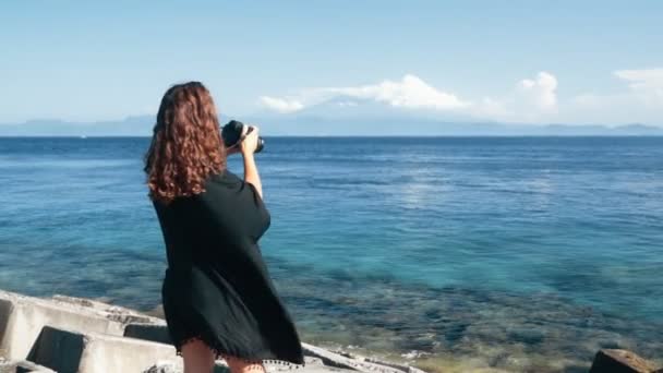 Vista posterior del lado de la chica fotógrafo toma fotos de océano, montañas, cámara lenta — Vídeo de stock