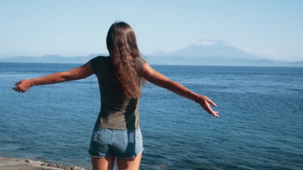 Girl traveler spreads her arms wide, enjoys view of ocean, mountains, slow motion — Stock Video