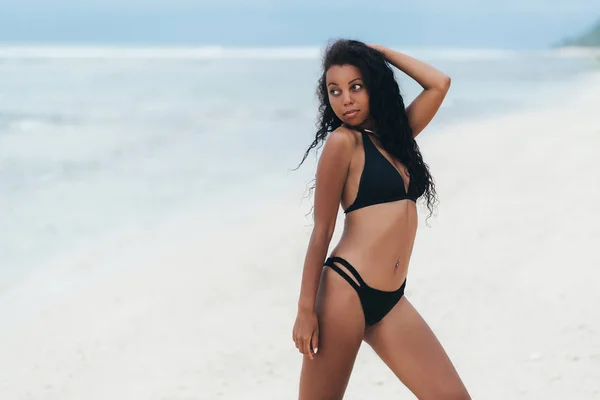 白い砂浜でポーズ水着で美しいセクシーな暗い肌の女の子、楽園の島で休むアフロアメリカの女性 — ストック写真