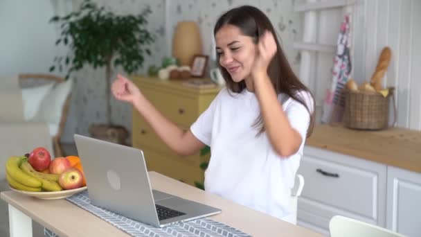 소녀는 노트북에서 일하고, 좋은 소식을 얻고, 기뻐하고, 웃고, 카메라를 보고, 슬로우 모션을 봅니다. — 비디오