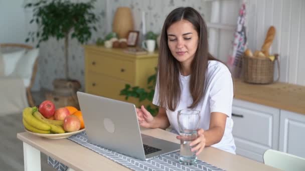 Довольно фрилансер женщина работает на ноутбуке, пьет чистую воду из стекла, замедленная съемка — стоковое видео