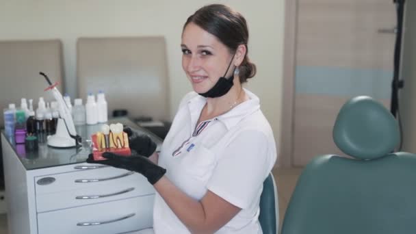 Mujer bonita dentista sonríe a la cámara y sostiene modelo de dientes en sus manos, cámara lenta — Vídeo de stock