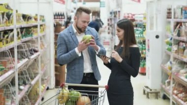 Kadın smartphone ürün ve adam listesi meyve seçer ve süpermarkette kokuyor denetlemek için kullanır.