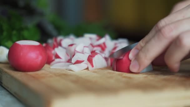 Fermer les mains de la femme avec des radis de coupe au couteau sur une planche en bois. Concept légume — Video