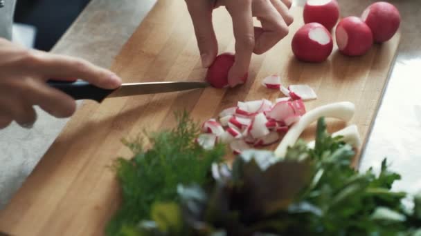 Fermer les mains de la femme au foyer avec des radis de coupe au couteau sur une planche en bois, ralenti — Video