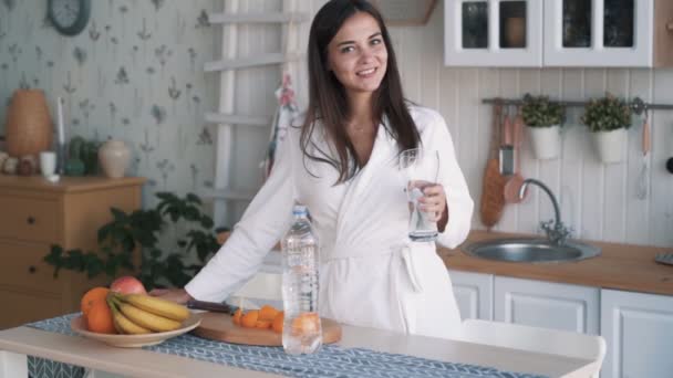 Meisje in badjas kijkt naar camera, glimlacht, drinkt water uit glas, Slow Motion — Stockvideo