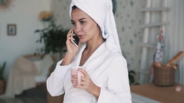 Başında havlu ile kız, telefonda konuşuyor, elinde fincan tutar, yavaş hareket